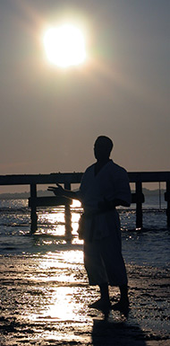 Il Maestro di karate Christian Gonzales y Herrera in kimono, con i piedi sulla battigia, sotto il sole del mattino